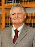 A man in suit and tie standing next to a book shelf.