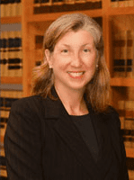 A woman in black jacket standing next to wooden bookcases.